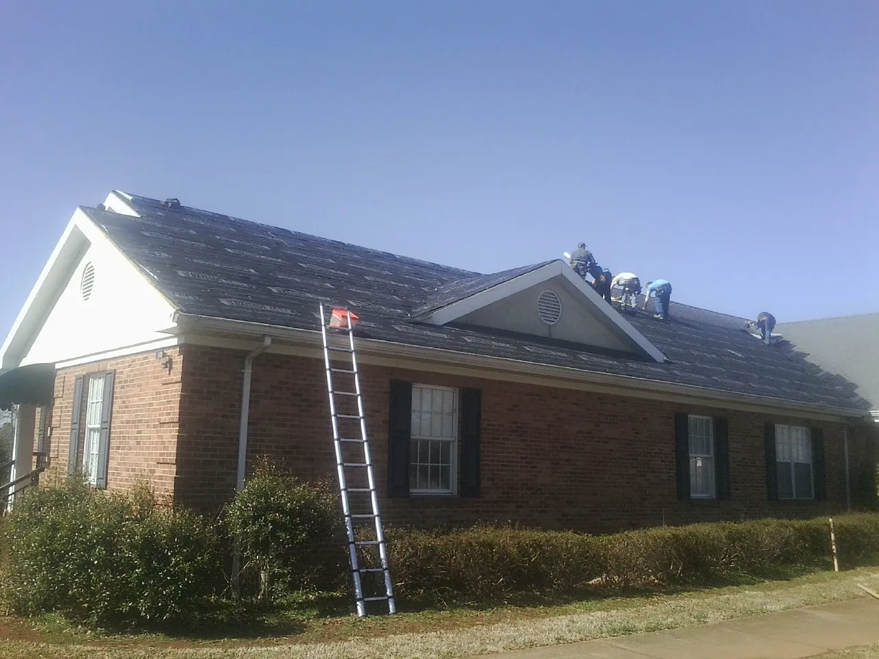 Crew tearing shingles off a brick ranch roof with a ladder set — Emergency Roof Repair work by our crew in Anderson